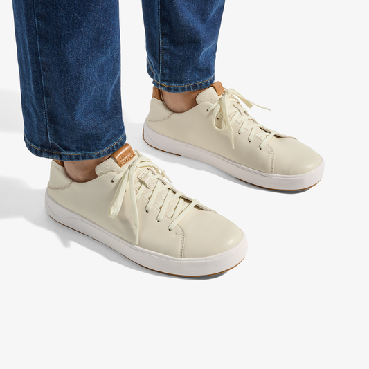 Cream-colored lace-up sneakers with white sole worn with rolled dark denim jeans.